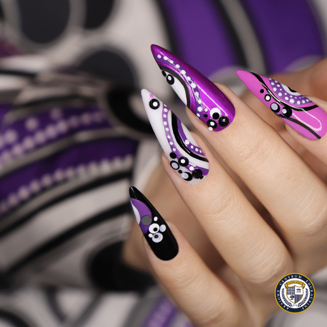 Zbliżenie na dłoń z efektownym, artystycznym zdobieniem na przedłużonych paznokciach w kształcie szpiców. Manicure w odcieniach fioletu, bieli i czerni ozdobiony geometrycznymi wzorami i kropkami. Tło kompozycyjnie dopasowane do stylu paznokci, tworzące harmonijną całość. W prawym dolnym rogu umieszczone logo