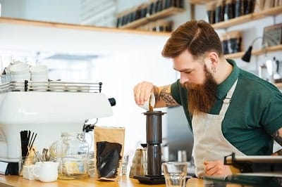 Barista parzy kawę w trakcie pracy, w tle kawiarnia