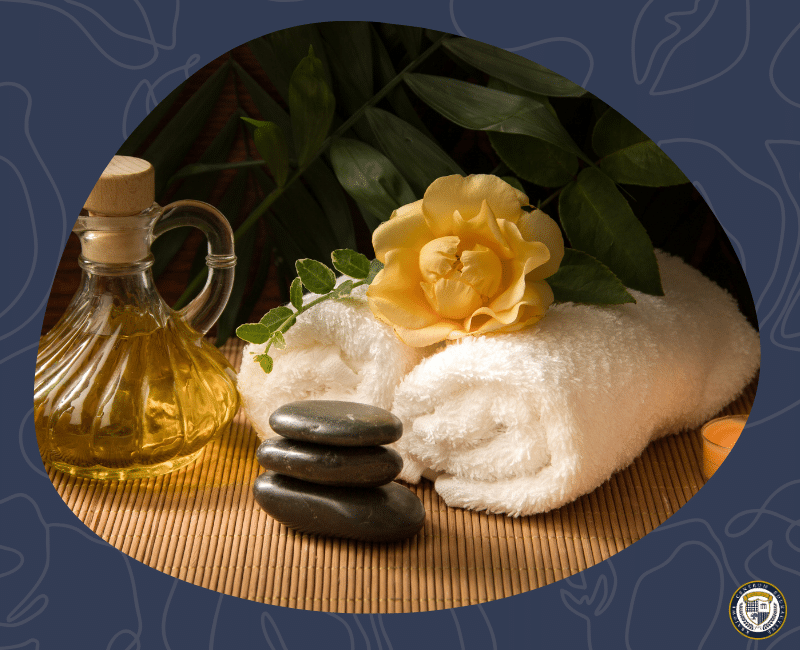Kompozycja spa z gorącymi kamieniami do masażu, aromatycznym olejkiem, białym ręcznikiem i żółtą różą na bambusowej macie