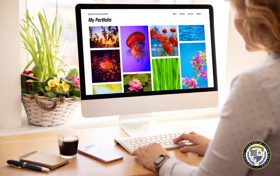 Kobieta siedzi przy biurku w jasnym wnętrzu i przegląda na dużym monitorze komputerowym kolorowe fotografie przyrodnicze w swoim portfolio, otoczone elementami dekoracyjnymi i kubkiem kawy.